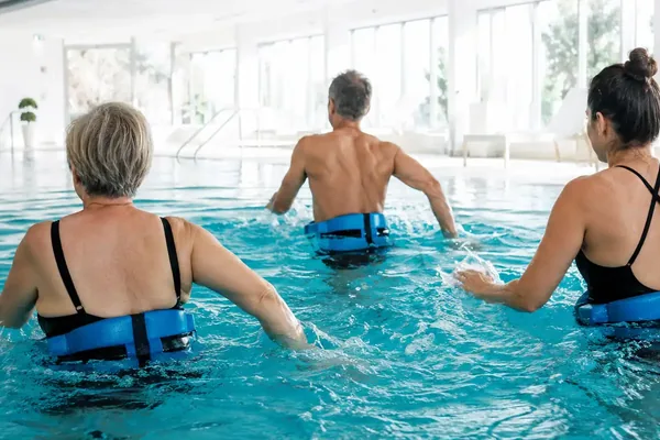Tre adulti di spalle, con la cintura galleggiante da Aquafit®, durante una lezione in vasca coperta — Aquafit®