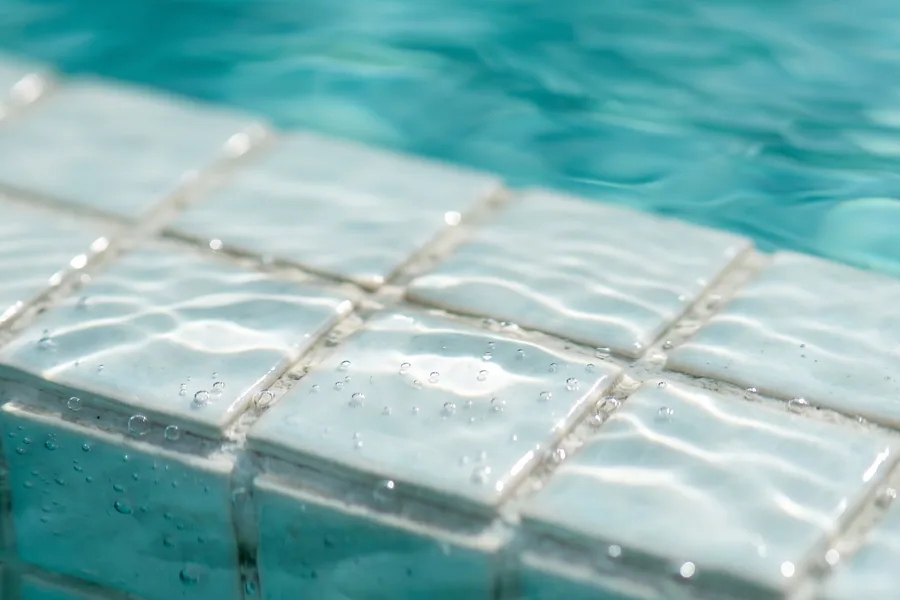 Il bordo piastrellato di una vasca a filo d’acqua, lambito dalla superficie
